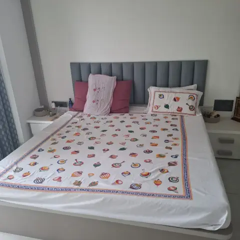 A grey channel-tufted floating bed with a colourful traditional block-print bedspread, flanked by white floating nightstands, against plain white walls.