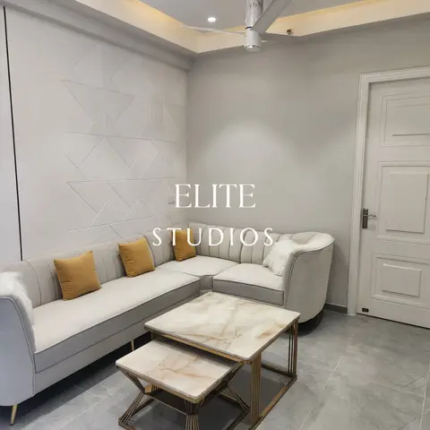 A grey channel-tufted L-shaped sofa with mustard cushions against a 3D geometric textured accent wall, with gold-framed marble nesting coffee tables.