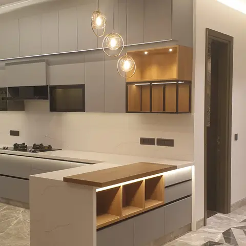 A grey handleless kitchen island with a walnut breakfast-bar top and open shelving, lit by three brass ring pendants