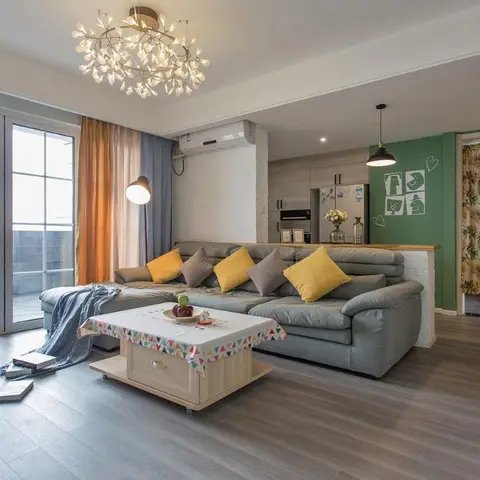 A grey L-shaped sofa with mustard cushions sits before floor-to-ceiling balcony doors