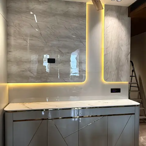 A grey marble-clad wall with a glowing LED light channel above a long grey console cabinet featuring brass diagonal inlay lines on the doors.