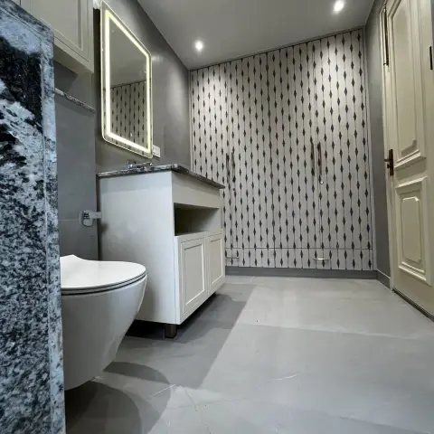 A grey-toned bathroom with a wall-hung WC, a granite-top floating vanity with a backlit LED mirror