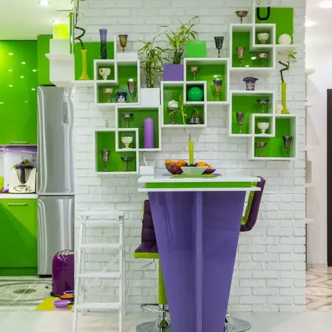 A high-gloss lime-green modular kitchen beside a white exposed-brick wall fitted with an asymmetric cubby shelf display of glassware