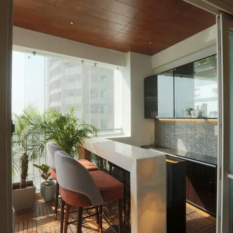 A high-rise balcony fitted out as a bar nook with a wood-clad ceiling, marble-topped counter, black glass overhead cabinet and geometric-tile backsplash