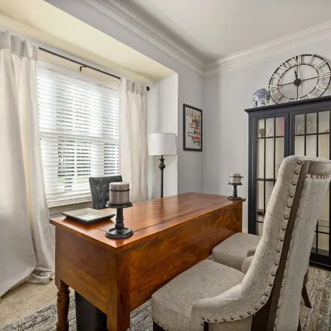 A home office nook with an antique wood writing desk, a nailhead-trim upholstered chair, and a black glass-front curio cabinet topped with a round wall clock