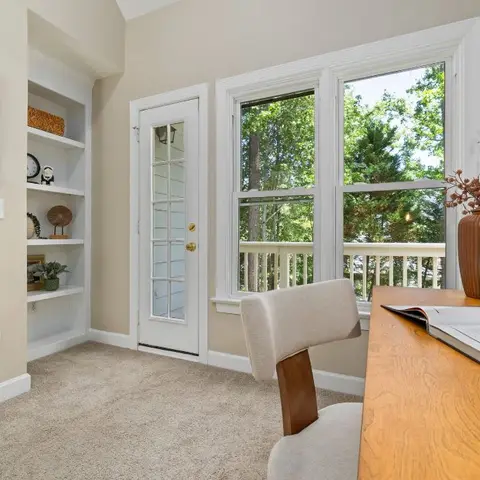 A home office nook with built-in alcove shelving, a paned glass door leading to a deck, and a wood desk with styled decor beneath a large window.