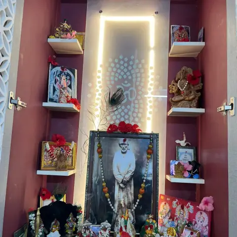 A home pooja unit interior with a backlit Om motif mirror panel, a framed photo of a saint with garlands
