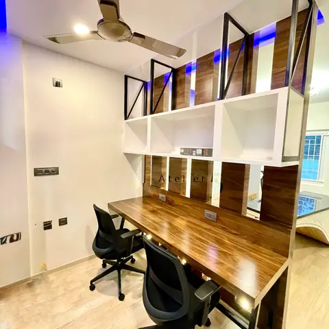A home study nook with a walnut-finish built-in desk and open-cube shelving unit framed in black metal, two mesh office chairs, and a ceiling fan.