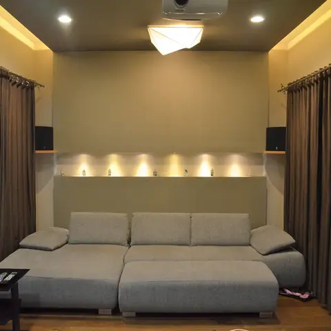 A home theatre-style living room with a grey L-shaped sofa facing a ceiling-mounted projector, a recessed lit display niche with decor figurines