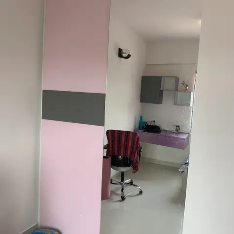 A kid's bedroom nook seen through a pink-and-grey wardrobe door, with a built-in lavender study desk and wall cabinets.