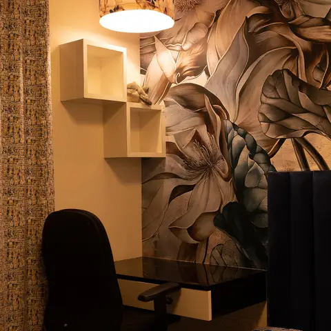 A kids' bedroom corner with a floating study desk against a large floral mural wallpaper, box shelving holding a plush toy, and a navy channel-tufted headboard.