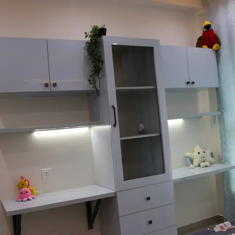 A kids' bedroom study-and-storage unit in white laminate with open shelves, a glass-door display cabinet, and under-shelf strip lighting