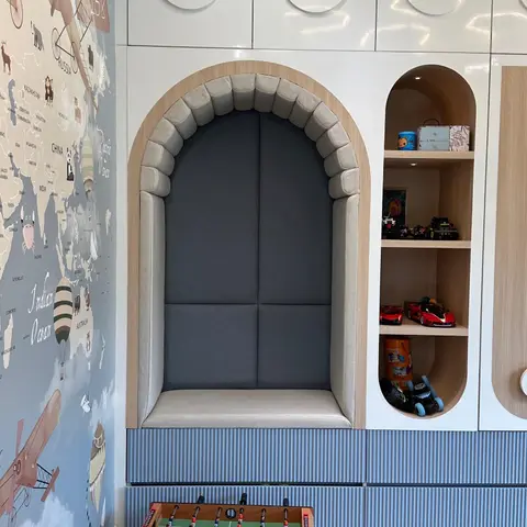 A kids' playroom nook with a cushioned arched reading bench built into wood-trimmed cabinetry, an airplane-themed world map wallpaper