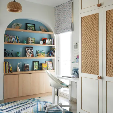 A kids' study nook with an arched blue-backed bookshelf, a built-in desk, a cane-front wardrobe with cat-shaped pulls, and a striped blue-green rug.