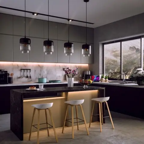 A kitchen island in black stone with a backlit kickboard, four black glass pendant lights above, light wood bar stools