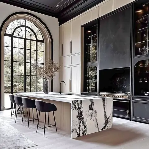 A kitchen island in book-matched waterfall marble with black bar stools, set against black lacquer cabinetry with glass-fronted uppers and brass hardware