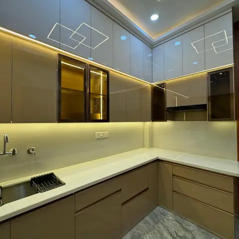 A kitchen with a glossy geometric-patterned false ceiling with cove and spot lighting, taupe high-gloss cabinets with lit glass display units
