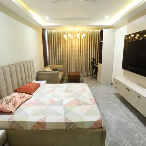A large master bedroom with a channel-tufted beige headboard wall, cove-lit ceiling