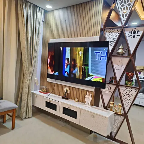 A laser-cut geometric wood-and-metal jaali room divider styled with brass idols and curios beside a fluted-panel TV wall.