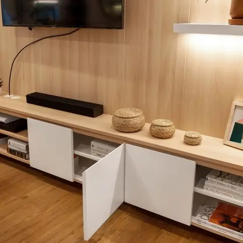A light wood-panelled TV wall with a floating console holding woven storage baskets, a framed abstract artwork, and open cabinet doors revealing books