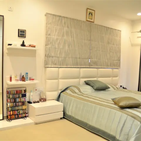 A lived-in bedroom with a tufted white headboard, a striped sage bedspread, and a bangle stand and grooming shelf beside a full-length mirror.