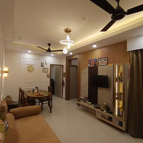 A living-dining room with a fluted wood-panel TV unit wall featuring a lit glass curio cabinet, a round wood dining table, a brown sofa