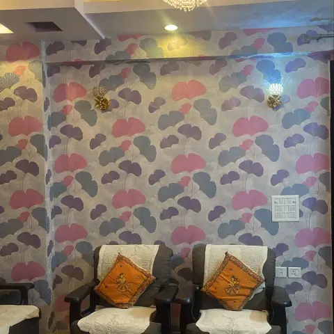 A living room accent wall in bold pink-and-purple ginkgo-leaf wallpaper, lit by a crystal chandelier and matching sconces