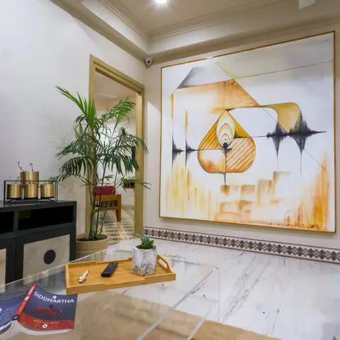 A living room corner with a large abstract oil painting on a beige wall, cream marble flooring bordered by a patterned mosaic tile strip