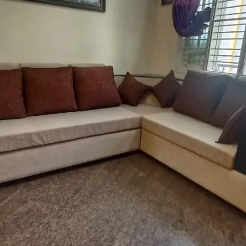 A living room corner with a cream L-shaped sectional sofa styled with maroon and brown scatter cushions