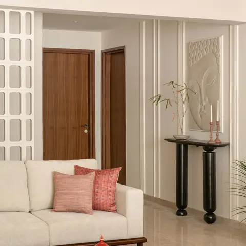 A living room corner with fluted plaster wall panelling, a carved stone Buddha-face wall relief above a black sculptural console table
