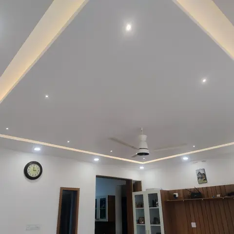 A living room dominated by a multi-tier pyramid POP false ceiling with perimeter cove lighting and a central fan