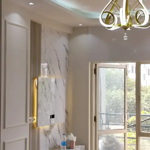 A living room feature wall in white-and-grey veined marble slab with backlighting, a gold crystal chandelier, and a floating white TV console below