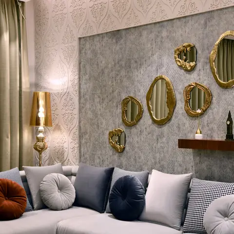 A living room sofa wall featuring a cluster of seven organic gold-rimmed mirrors on a textured grey stone-look panel, embossed damask wallpaper