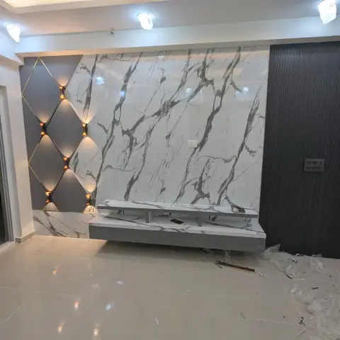 A living room TV feature wall with book-matched white marble cladding, a gold diamond-pattern accent light panel, and a fluted dark grey side panel