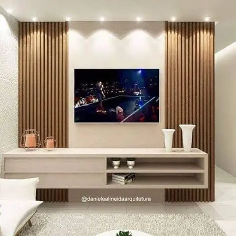 A living room TV feature wall with vertical fluted wood panelling either side, spotlighting above, and a floating cream console styled with vases and candles.