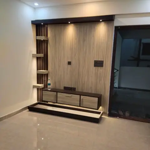 A living room TV feature wall with wood-veneer paneling, fluted corner display shelves, and a floating wood console below spotlighting.
