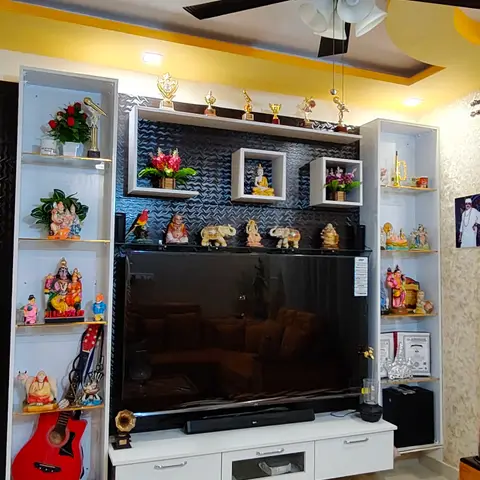 A living room TV unit with a textured black accent wall and cubby shelves crowded with figurines, trophies and a red guitar