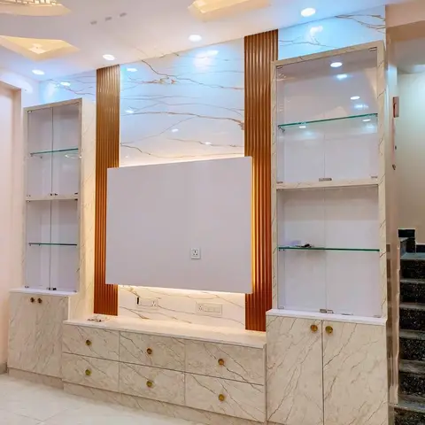 A living room TV wall clad in book-matched beige marble slabs with fluted gold-toned metal inserts