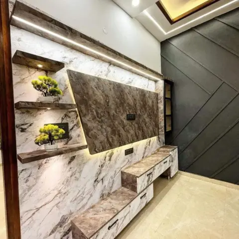 A living-room TV wall clad in book-matched brown-veined marble with backlit floating shelves for bonsai plants and a matching marble-finish console