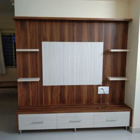 A living-room TV wall in two-tone wood laminate panelling with floating display shelves and a three-drawer TV console