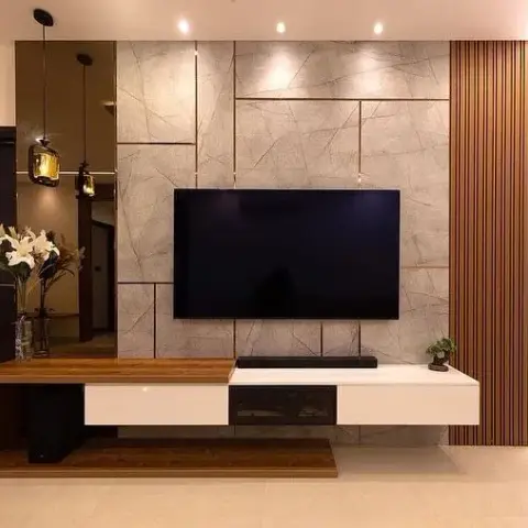 A living room TV wall with brass-inlaid grey marble panelling, backlit fluted wood cladding, and a floating walnut-and-white console.