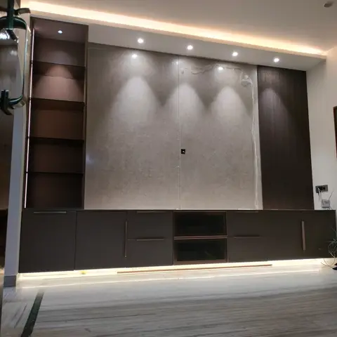 A living room TV wall with a large stone slab panel (still under protective film) beside a dark fluted wood strip