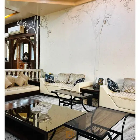 A living room with a 3D textured tree mural on the end wall, a gold cove-lit tray ceiling, cream leather sofas