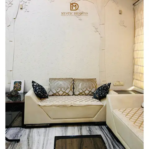 A living room with a 3D textured stucco tree-branch feature wall behind a cream tufted sofa set with gold-patterned and navy accent cushions, on marble flooring