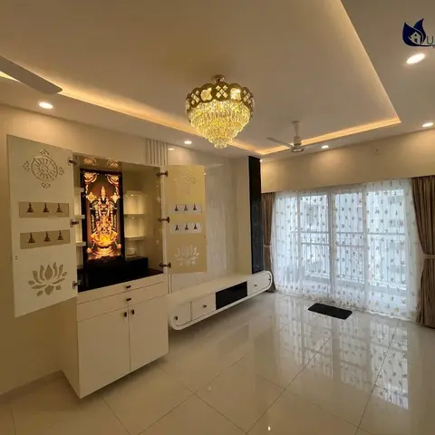 A living room with a backlit pooja alcove featuring lotus-motif cutout doors, a floating white TV console, and a crystal chandelier over a glossy tile floor.