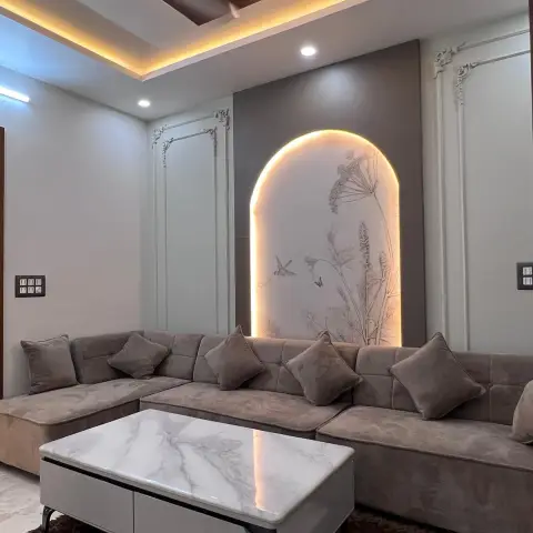A living room with a backlit arched wall panel featuring botanical line-art, flanked by ornate wall moulding, a grey tufted L-shaped sofa