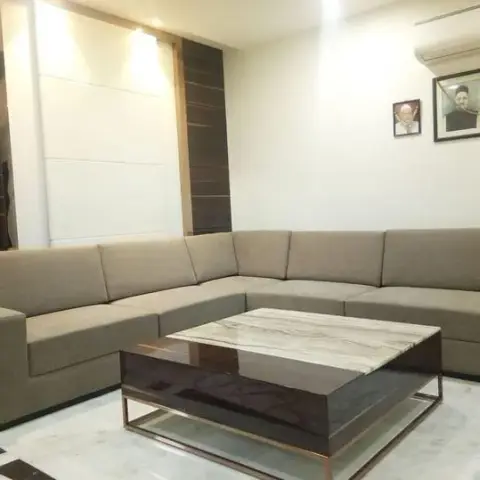 A living room with a beige L-shaped sectional sofa and a marble-top coffee table with brass trim, set against a dark wood and light-panel accent wall.