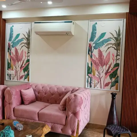 A living room with a blush-pink tufted velvet sofa set against framed botanical wallpaper panels flanked by fluted wood pilasters.