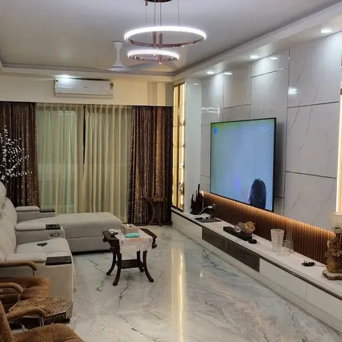A living room with a book-matched marble TV wall flanked by fluted wood-and-brass columns, beneath a double-ring chandelier
