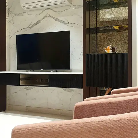 A living room with a book-matched marble TV wall, a black fluted-texture media console, and blush pink boucle sofas in the foreground.